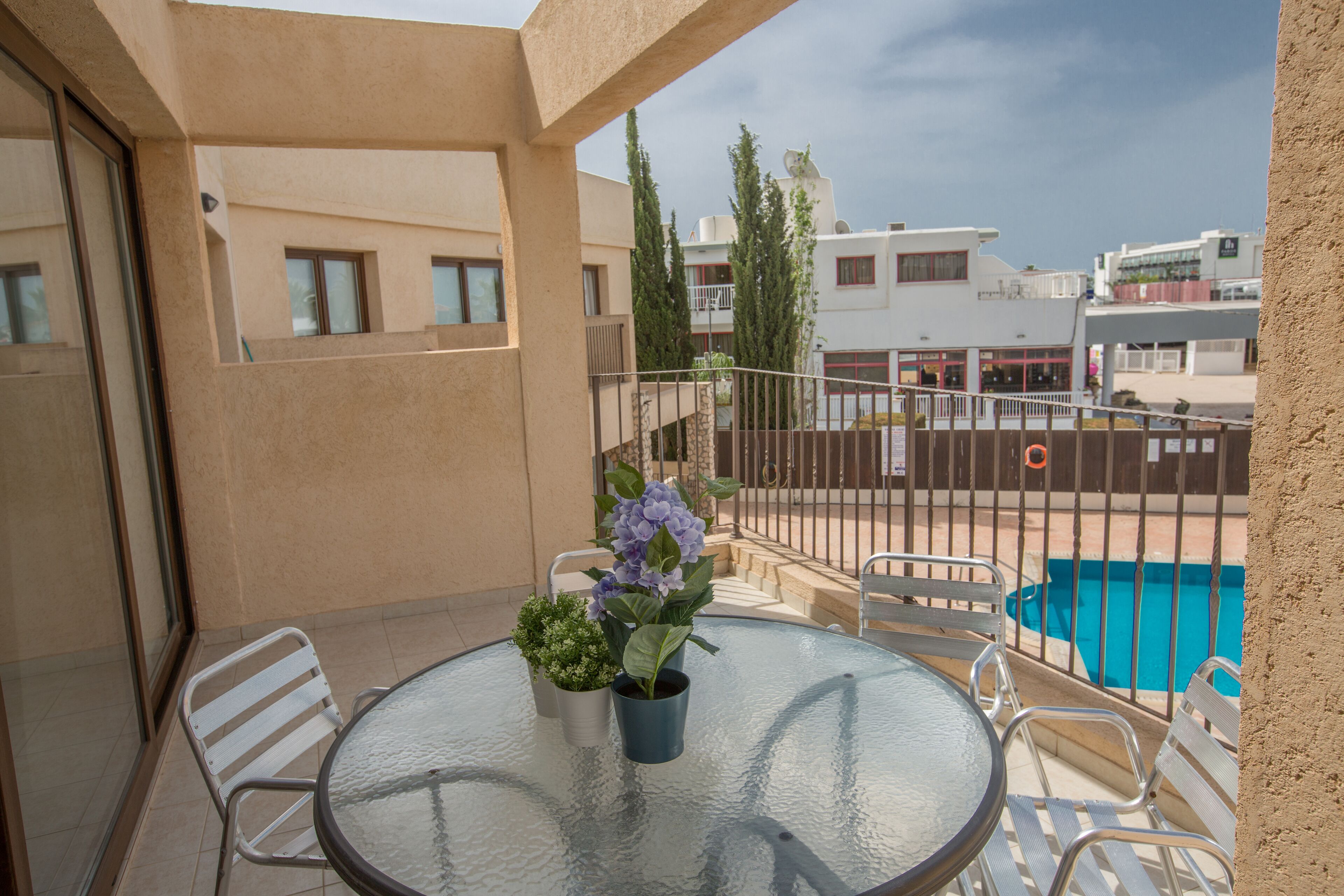 A balcony with a glass table, chairs, and potted plants.