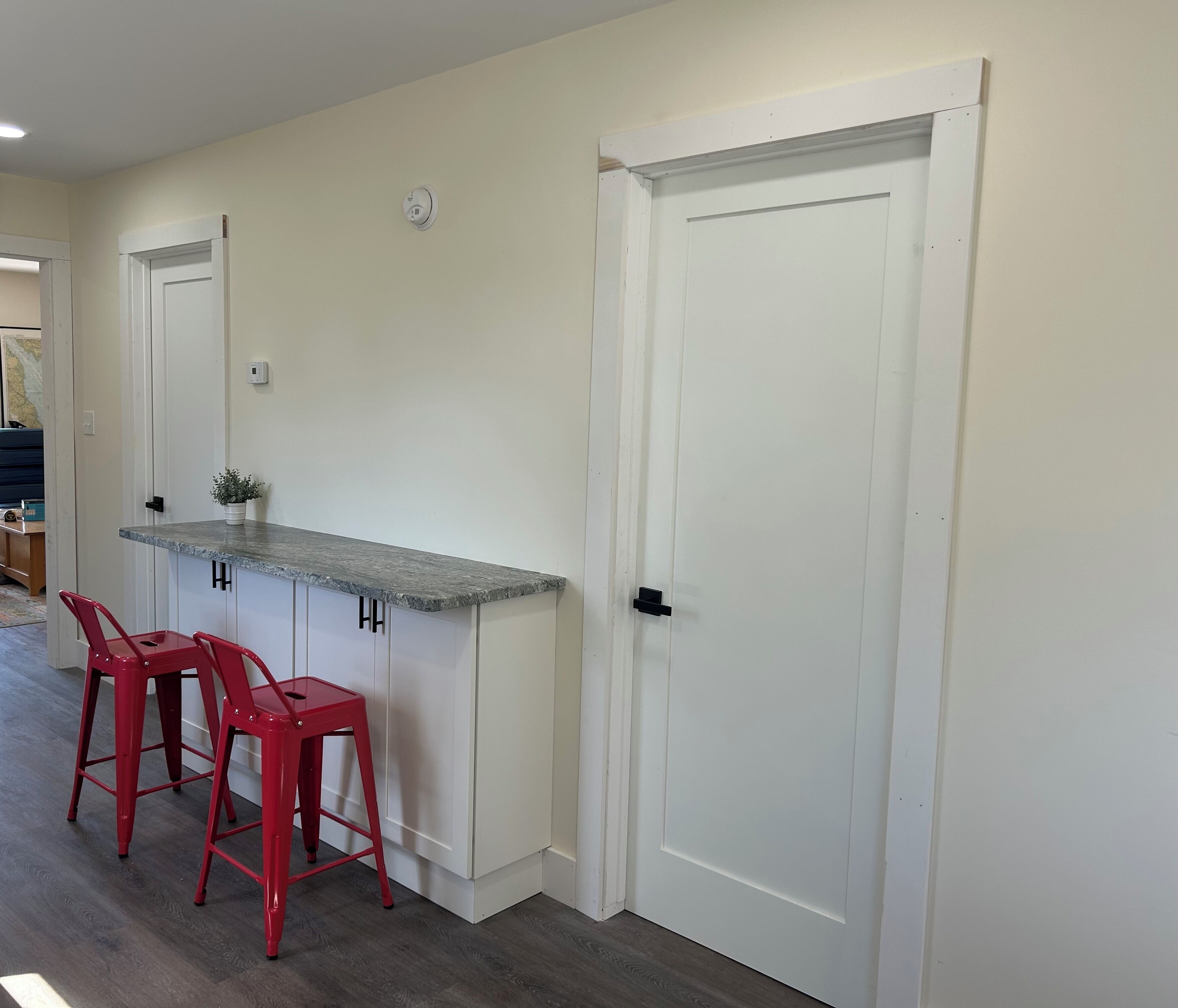 A kitchen with a white countertop, two red bar stools, and a white door.