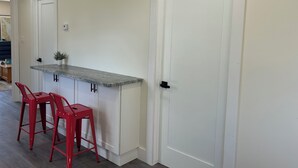 Uma cozinha com bancada branca, dois bancos altos vermelhos e uma porta branca.