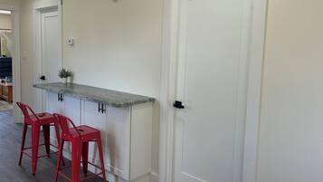 A kitchen with a white countertop, two red bar stools, and a white door.