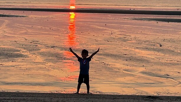 Criança em uma praia, de frente para o pôr do sol.