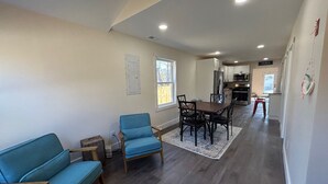 Uma sala de estar ampla com um sofá azul, uma mesa de jantar com cadeiras e uma cozinha ao fundo.