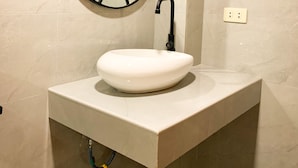 Casa de banho com uma pia branca, um espelho redondo e um porta-toalhas.