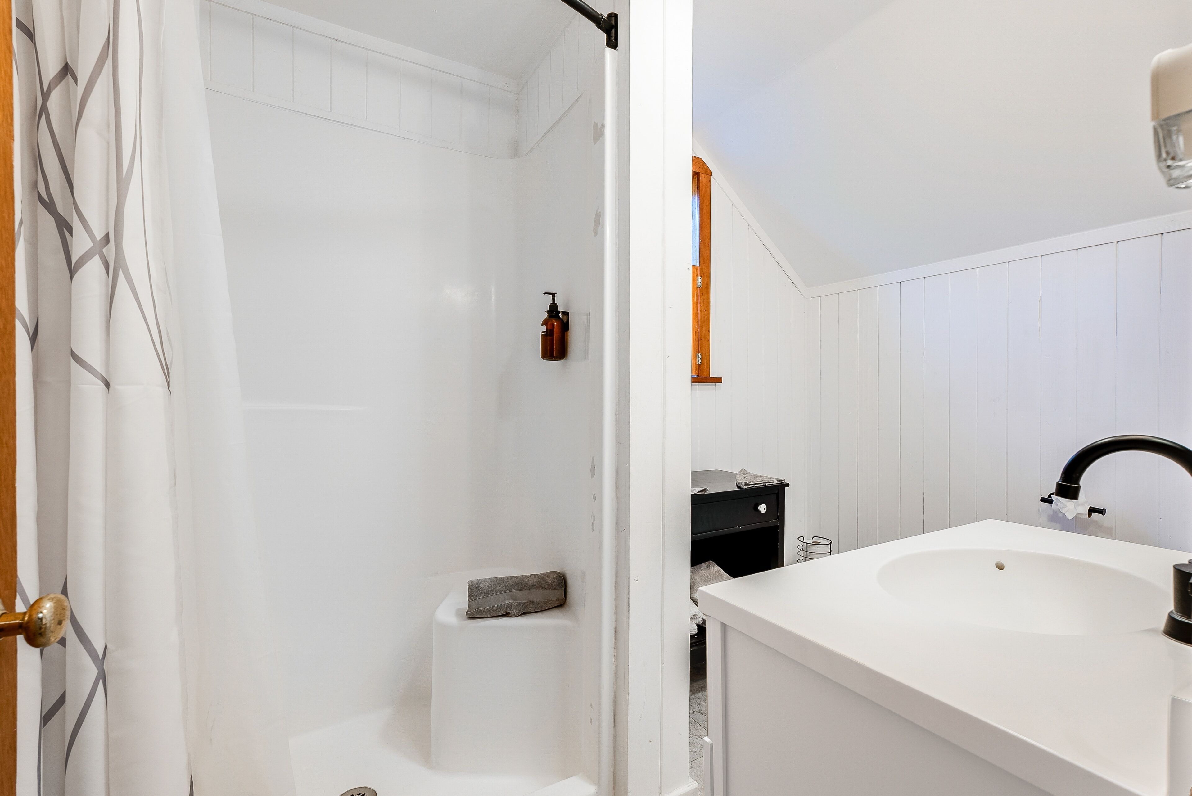 Un baño con un lavamanos blanco, un grifo negro, una zona de ducha y una puerta de madera.