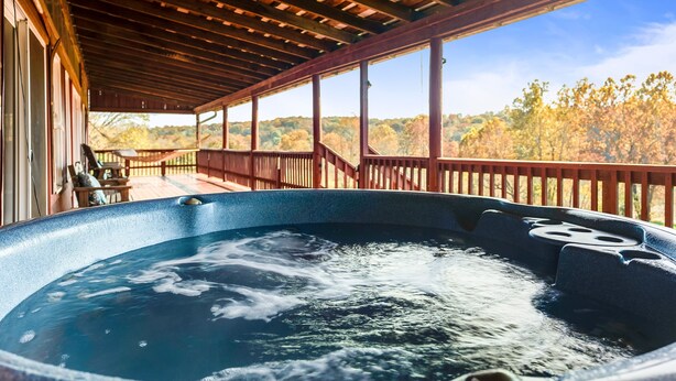 A hot tub under a wooden deck with a view of autumn trees.