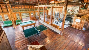 A spacious indoor area with wooden floors, a ping pong table, and a stone fireplace.