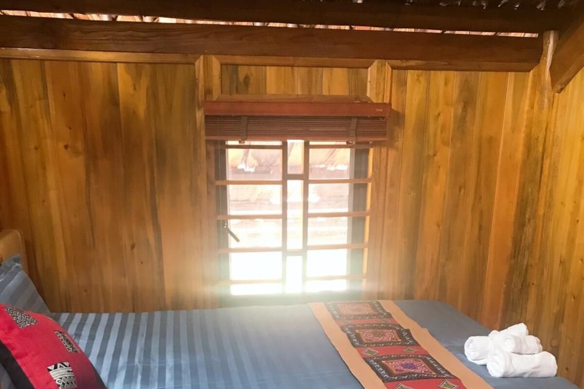A wooden cabin room with a bed, a window, and a wooden ceiling.