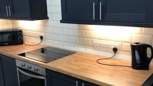 A modern kitchen with dark cabinets, a microwave, a stove, and a kettle.