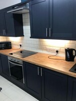 Una cocina moderna con armarios oscuros, microondas, estufa y hervidor.