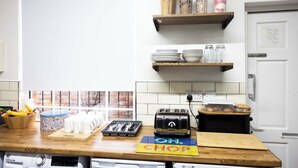A kitchen with a wooden countertop, a toaster, a cutting board, and various kitchen utensils. There are shelves above the counter holding jars and a can of oats.