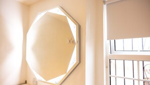 A room with a large octagonal mirror on the wall, a window with metal bars, and a white door.