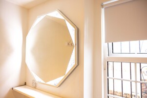 Una habitación con un espejo octogonal grande en la pared, una ventana con barrotes y una puerta blanca.