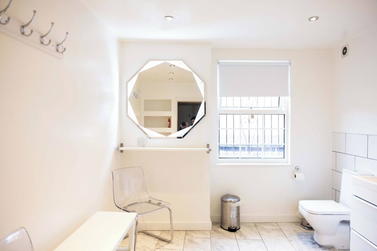Un bagno con un lavandino bianco, un water, uno specchio, una finestra con sbarre e un cestino.