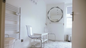 A bathroom with a white sink, a mirror with a decorative frame, a white chair, and a trash bin.
