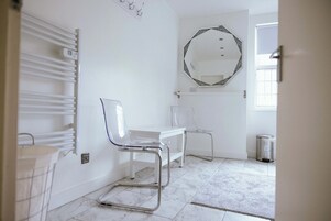 Un baño con un lavamanos blanco, un espejo con marco decorativo, una silla blanca y un cubo de basura.