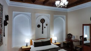 A hotel room with a large bed, two bedside tables with lamps, a wooden ceiling, and a chandelier.