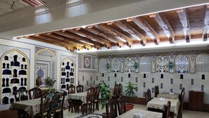 A restaurant with traditional decor, featuring patterned walls, wooden ceiling beams, and multiple tables with chairs.