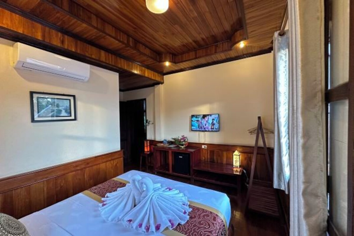 Une chambre d’hôtel avec un plafond en bois, un lit recouvert d’une courtepointe blanche et rouge, un téléviseur fixé au mur et un bureau avec une lampe.