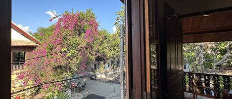 Vista desde un balcón con una señal de pare, un árbol de flores rosadas y un cielo azul despejado.