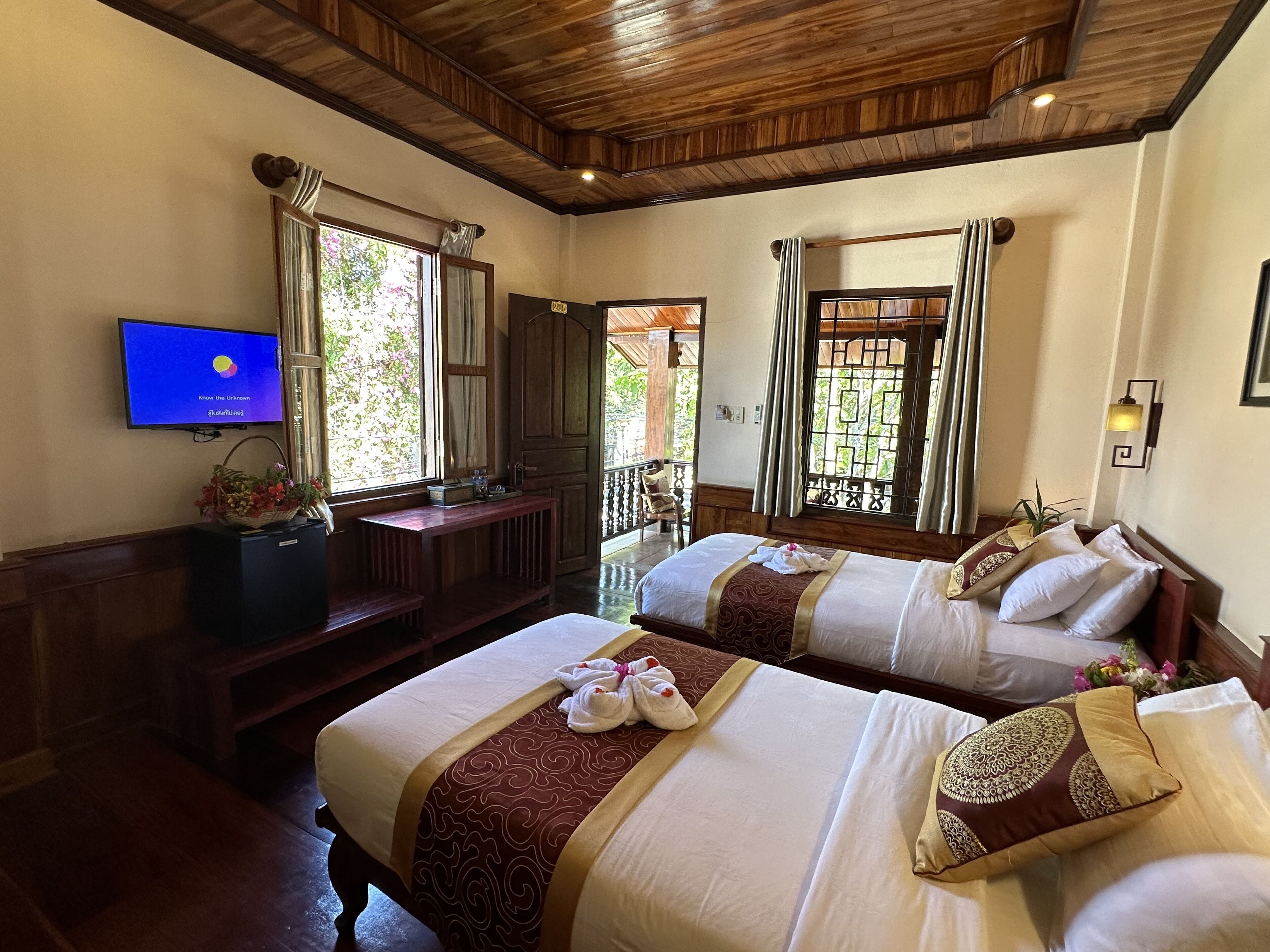 Une chambre d’hôtel avec deux lits, une télévision et un balcon donnant sur un espace verdoyant.