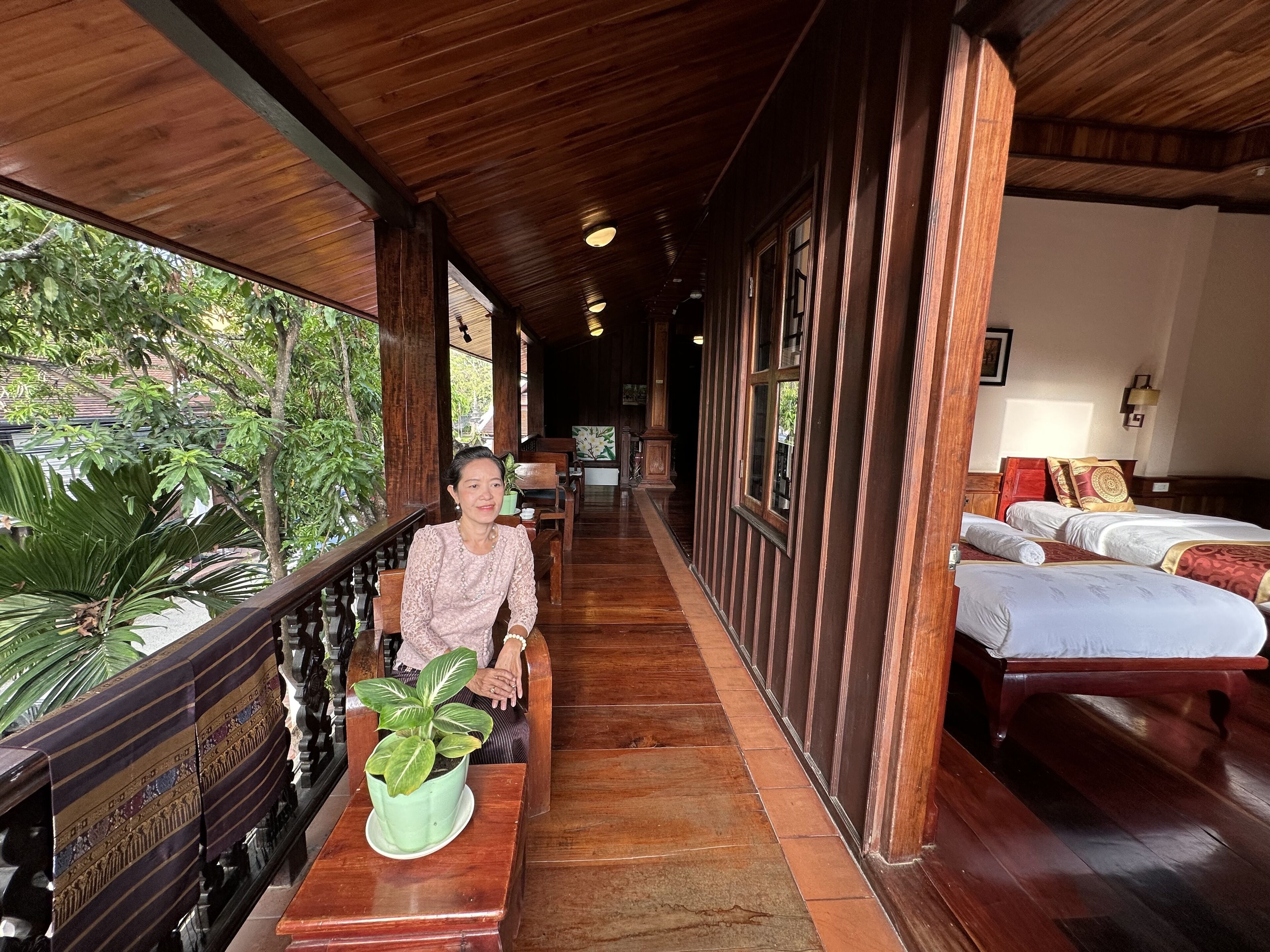 A corridor with wooden flooring, a seating area with a table and chairs, and a bed with a patterned bedspread.