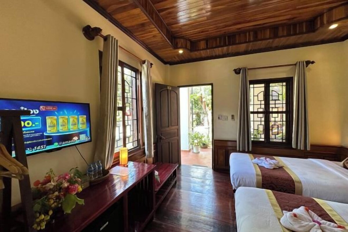 A hotel room with a wooden ceiling, two beds, a TV, and a window with curtains.