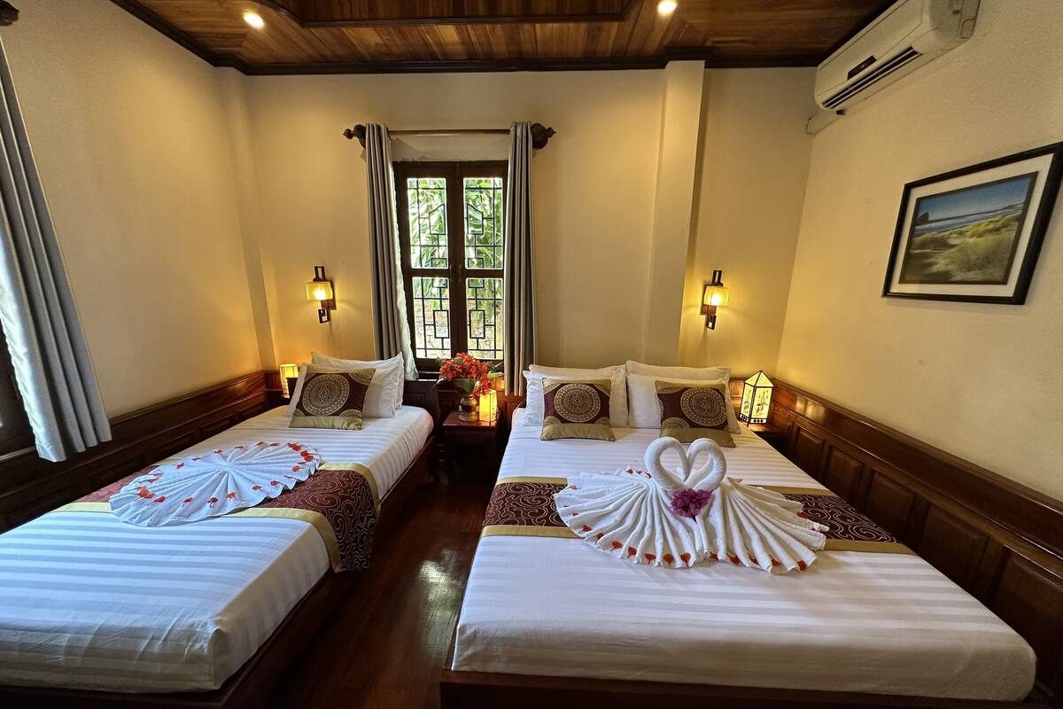 Een hotelkamer met twee bedden, elk voorzien van handdoeken gevouwen in de vorm van een hart, houten hoofdeinden en een raam met gordijnen.