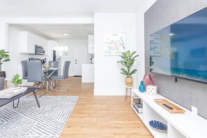 A modern living room with a dining area, a kitchen in the background, and a large TV mounted on the wall. - Modern two bedroom house with large outdoor space  (Miami)