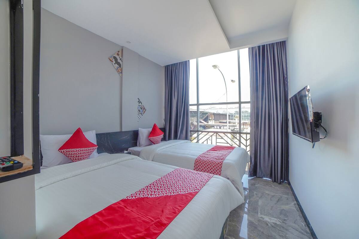 Ein Hotelzimmer mit zwei Betten, einem Fernseher und einem Fenster mit Vorhängen.