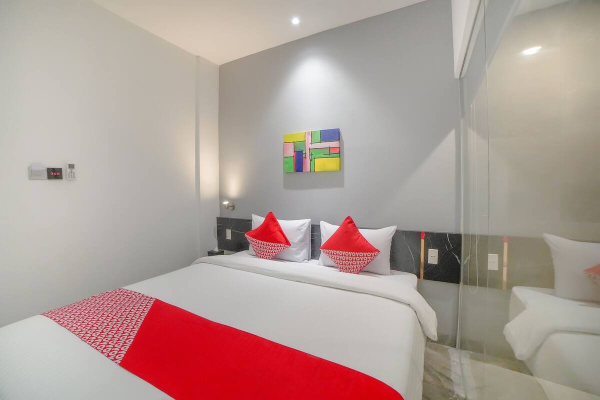 Ein modernes Hotelzimmer mit einem großen Bett, einer Glastrennwand und einem farbenfrohen abstrakten Gemälde an der Wand.
