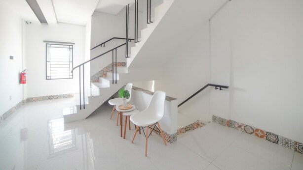 A modern interior with a staircase, white walls, and a dining area with white chairs and a small table. - Capital O 90447 Kardopa Hotel Megapark (Medan)