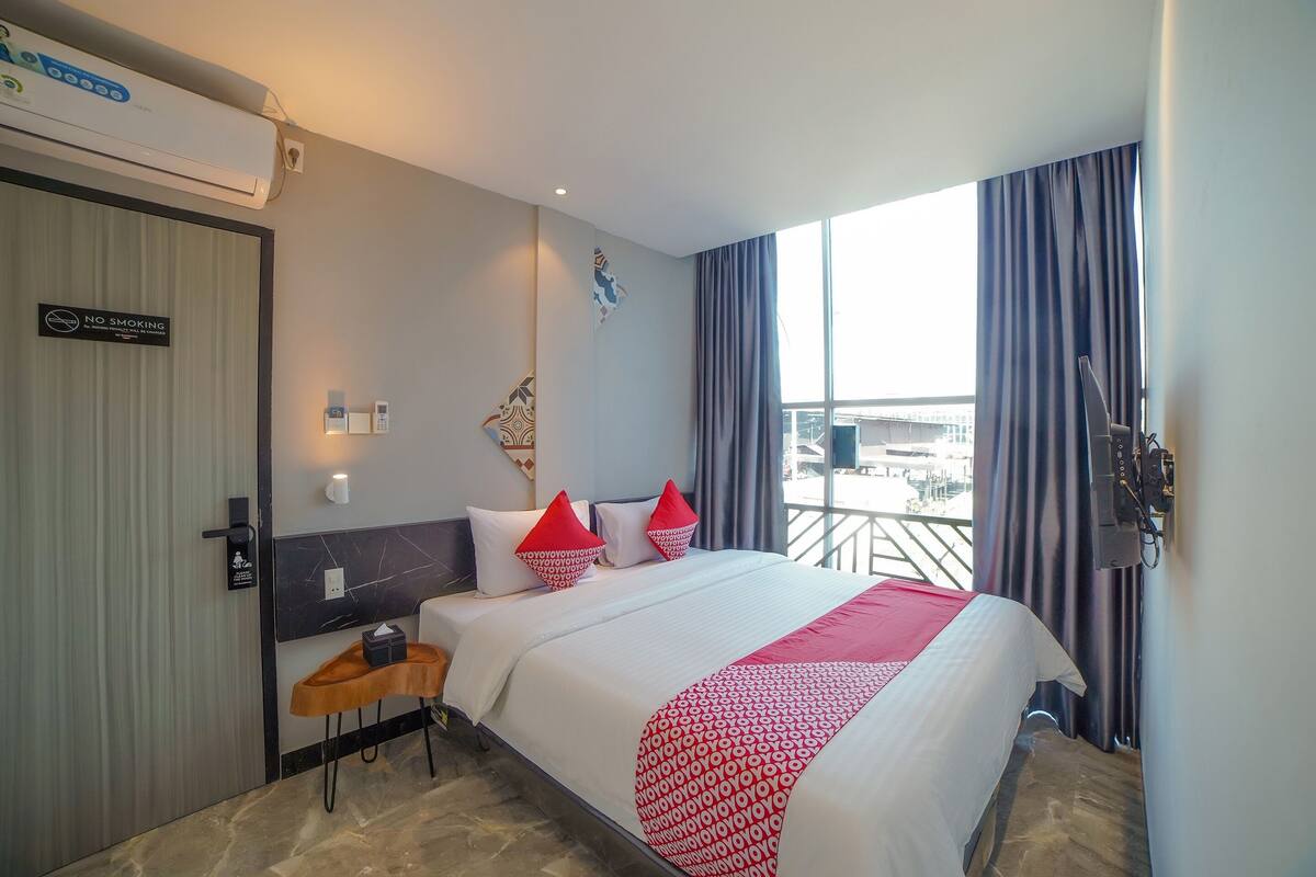 Ein Hotelzimmer mit Bett, kleinem Tisch, Fernseher und einem Balkon mit Vorhängen.