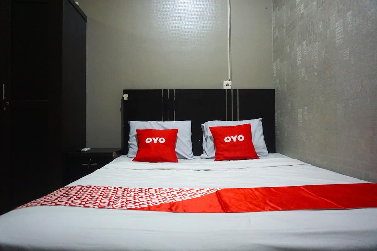 A hotel room with a bed, two red pillows with "OYO" branding, a white bedspread, and a red blanket.