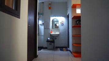 A narrow hallway with a sink, mirror, and shelves.
