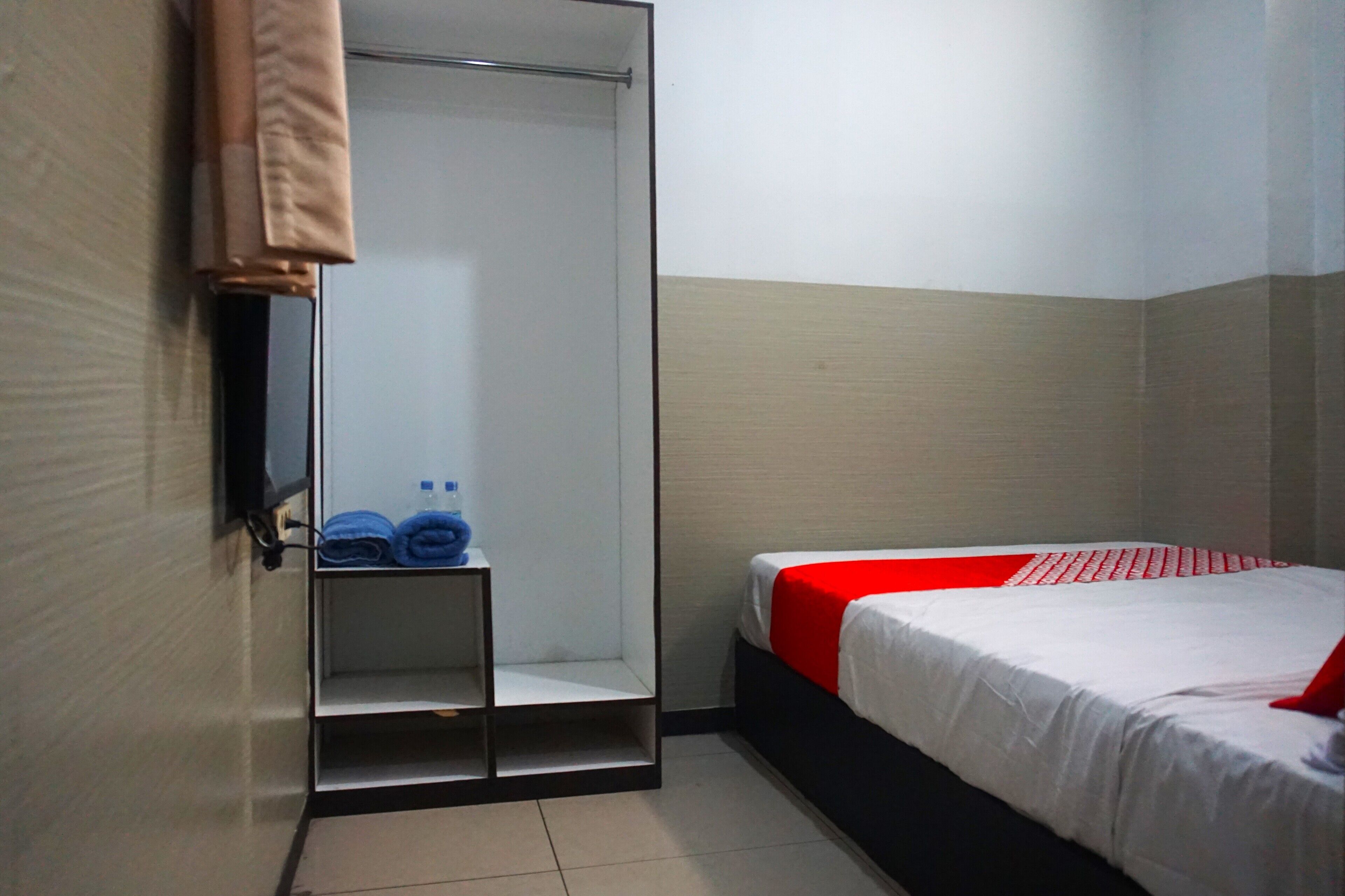 Camera d'albergo con un letto, un armadio e uno scaffale con asciugamani piegati.