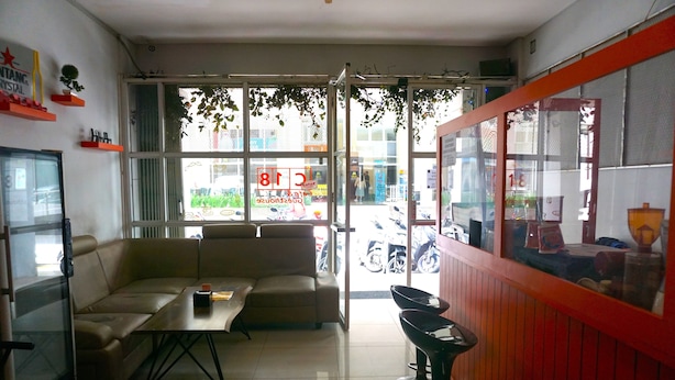 A room with a sofa, a table, a TV, and a window with a view of the street. - Capital O 3952 Hotel C 18 Cibaduyut (Bandung)