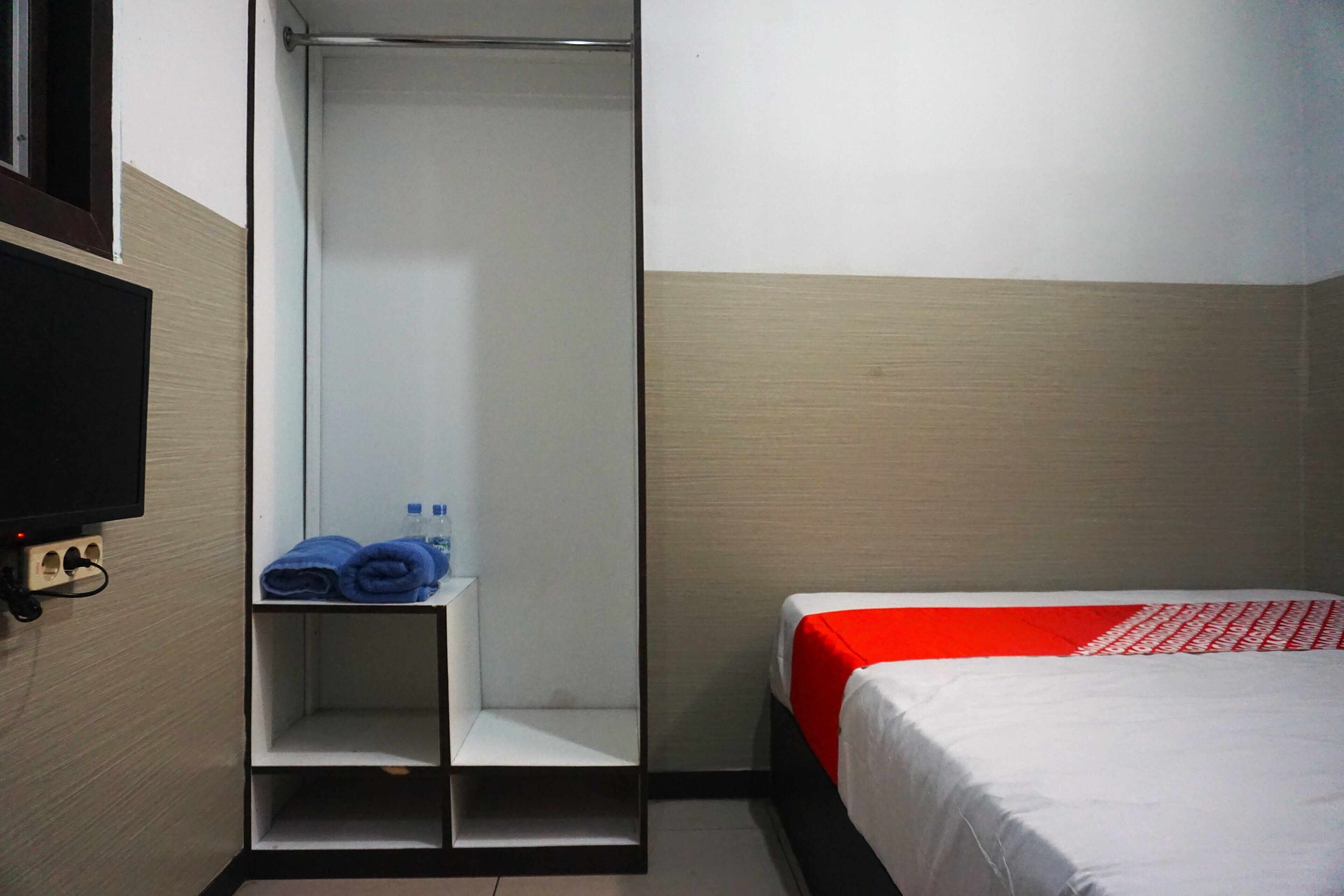 A hotel room with a bed, a shower area, and a television mounted on the wall.