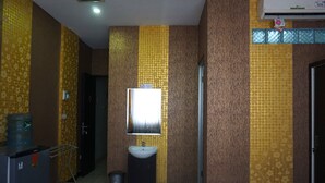 A bathroom with a sink, mirror, and toilet. There is a trash can and a water dispenser. The walls have a patterned wallpaper. - Capital O 3952 Hotel C 18 Cibaduyut (Bandung)