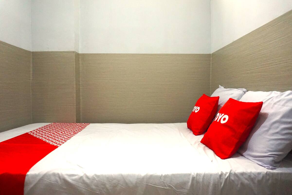 A hotel room with a bed, a red and white bedspread, and two red pillows with the word "YOYO" on them.