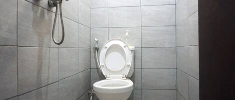 A small, tiled bathroom with a toilet, a handheld showerhead, and a toilet paper dispenser.