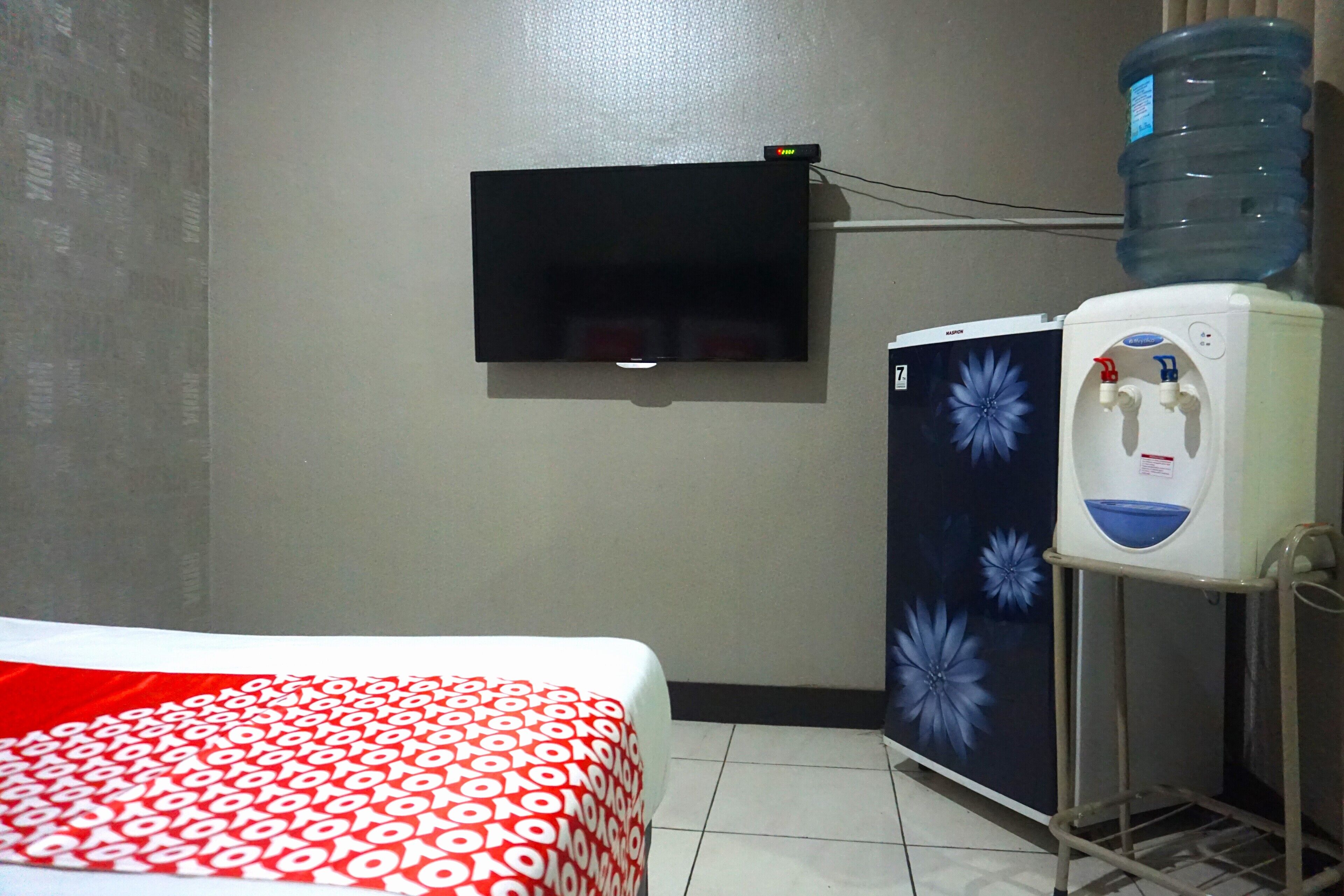 Ein Hotelzimmer mit einem Bett, einem an der Wand montierten Fernseher und einem Wasserspender.
