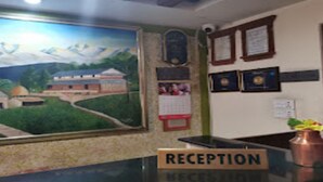 Zona de recepción con un cuadro de un paisaje, señal de recepción, certificados enmarcados y un jarrón con flores.