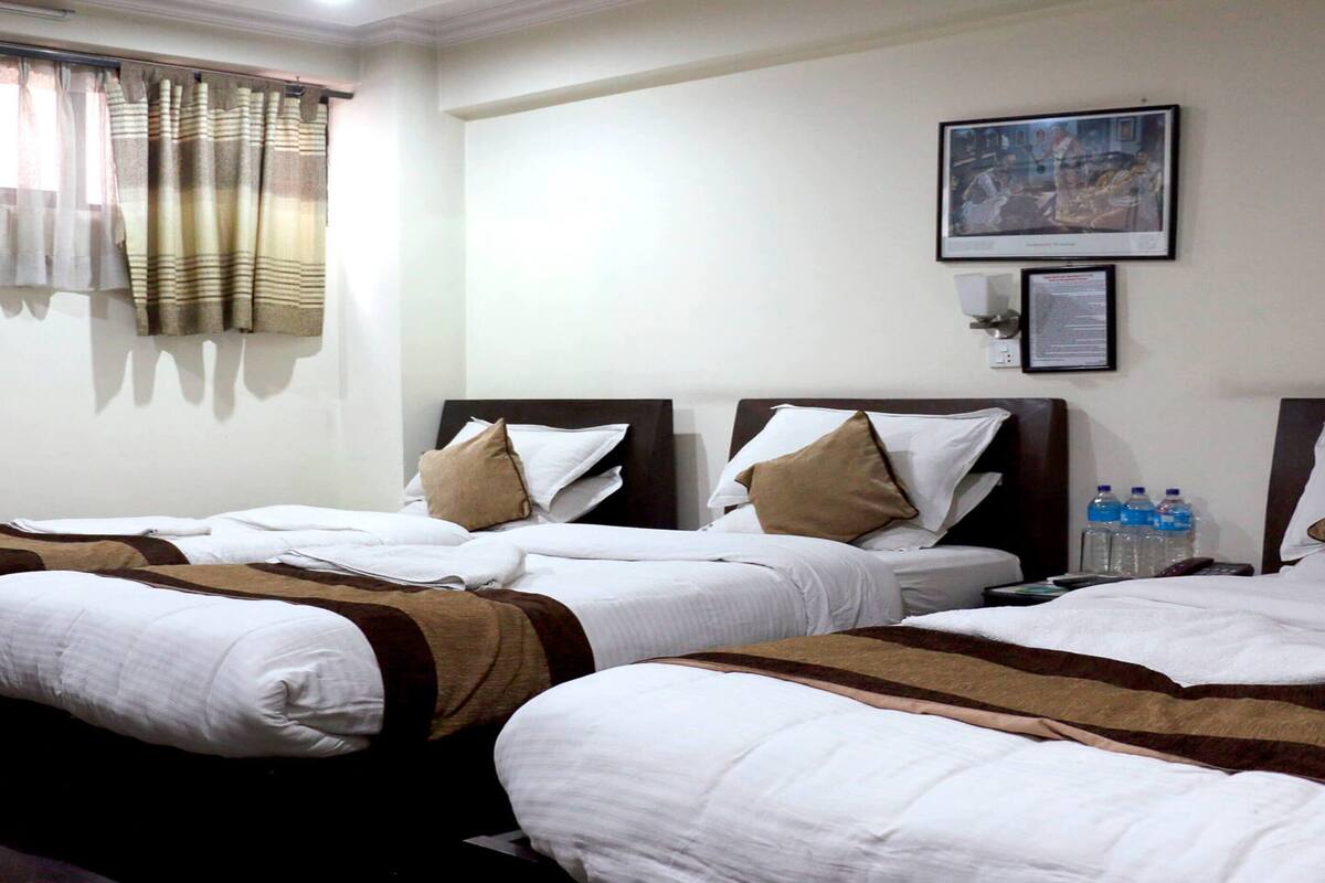 A hotel room with two beds, each with white bedding and brown accents, a window with striped curtains, and a framed picture on the wall.