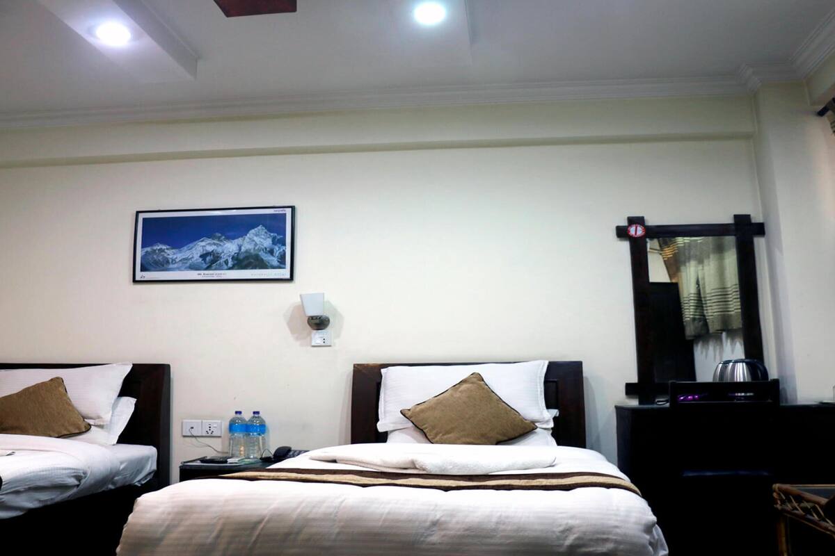 A hotel room with two beds, a mounted TV, a wall-mounted heater, and a window with curtains.