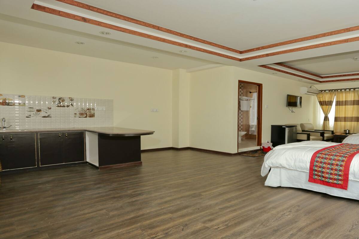 A hotel room with a large bed, a desk, and a kitchenette.