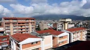 Un paisaje urbano con edificios de varios pisos, algunos con balcones, y montañas al fondo.