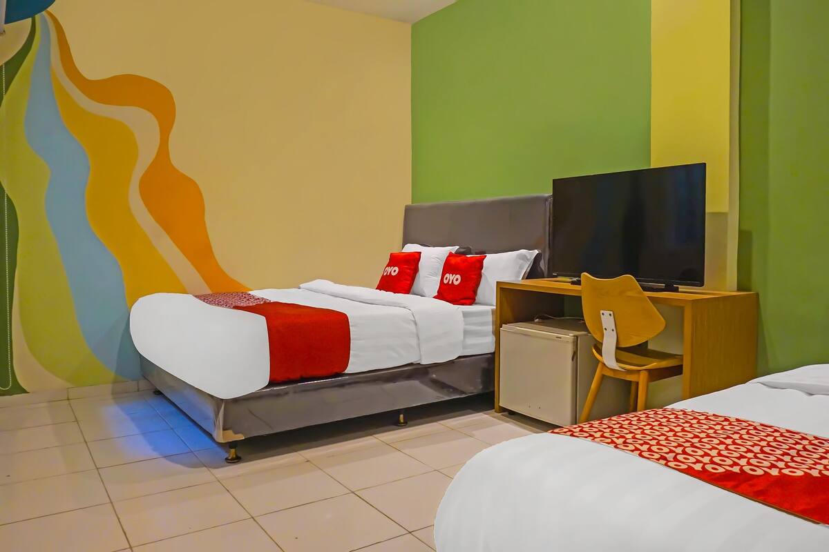 A hotel room with a bed, a desk with a chair, a television, and a small refrigerator.