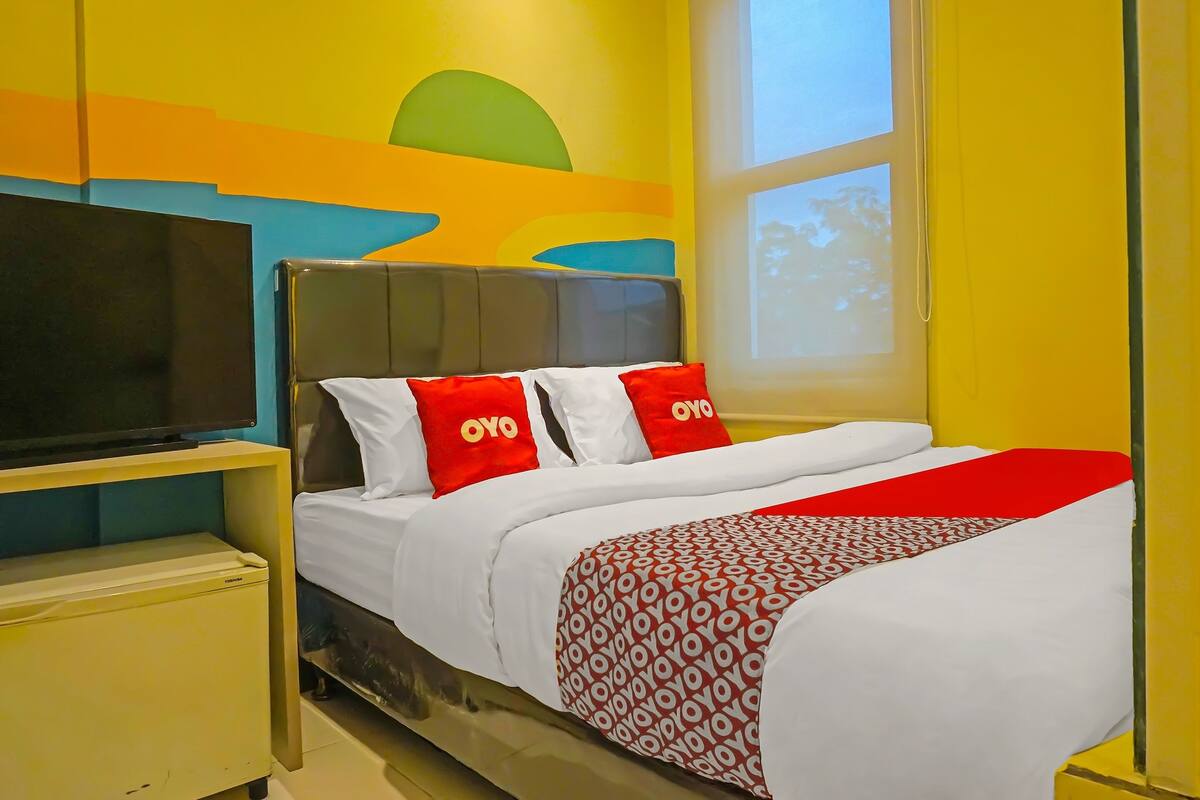 A hotel room with a bed, a TV on a stand, and a window with a view of trees.