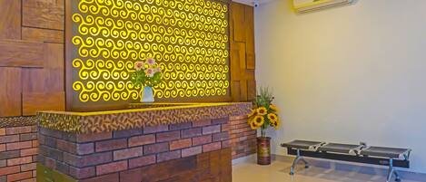 A reception area with a wooden reception desk, a decorative wall with yellow patterns, and a bench with sunflowers.