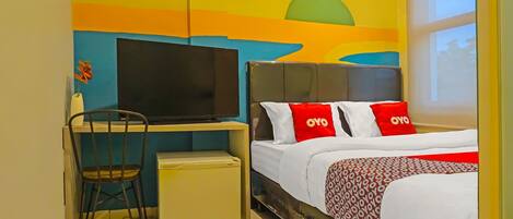 A hotel room with a bed, a desk with a chair, a television, and a wall with a colorful mural.